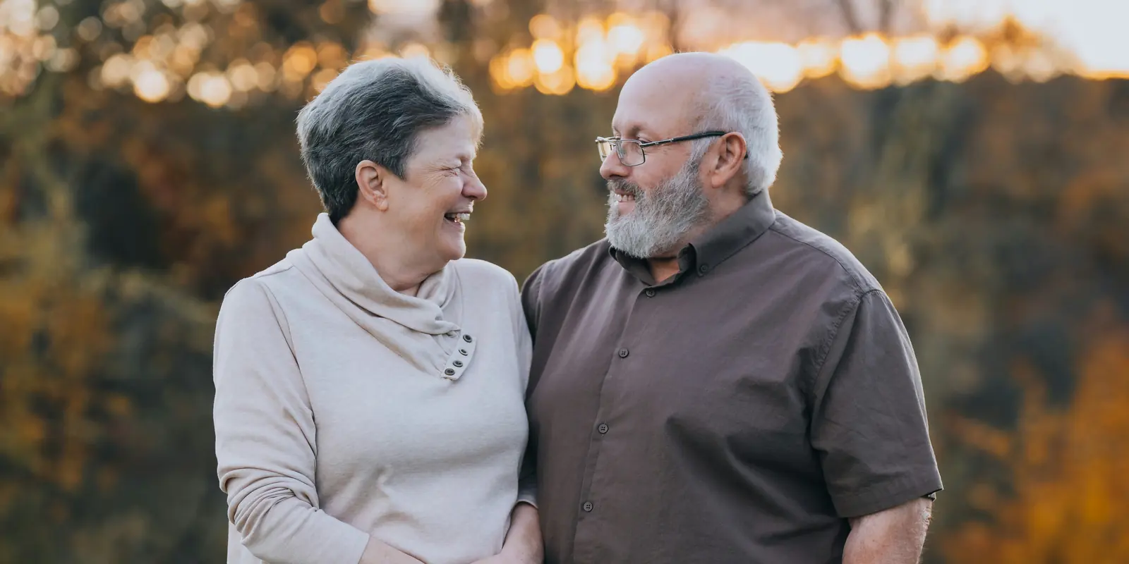 An older couple laugh together outdoors at sunset