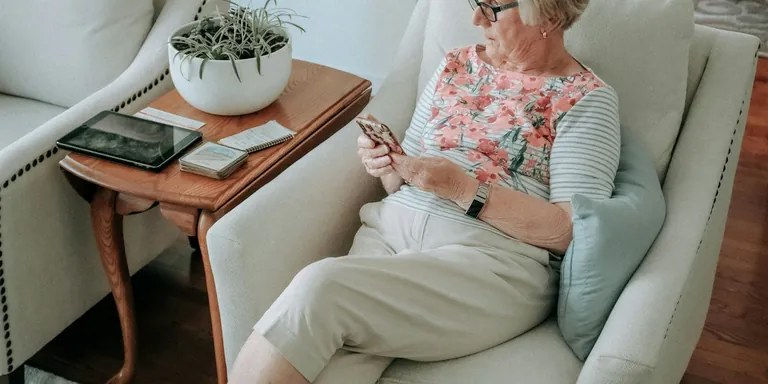 An older woman seated in an armchair at home reading on her phone