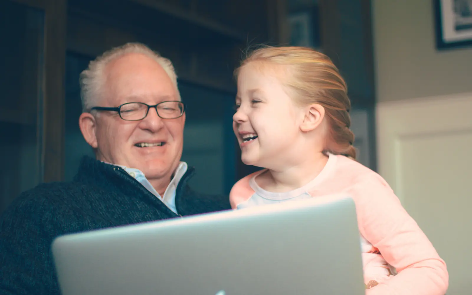 A grandfather and his granddaughter laughing together at a laptop